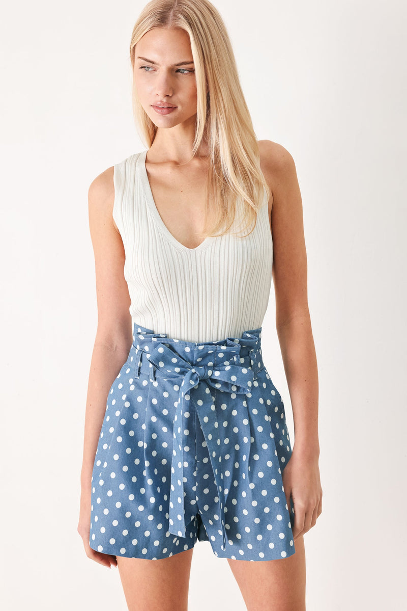 Woman wearing a white sleeveless top and blue polka dot shorts on a white background