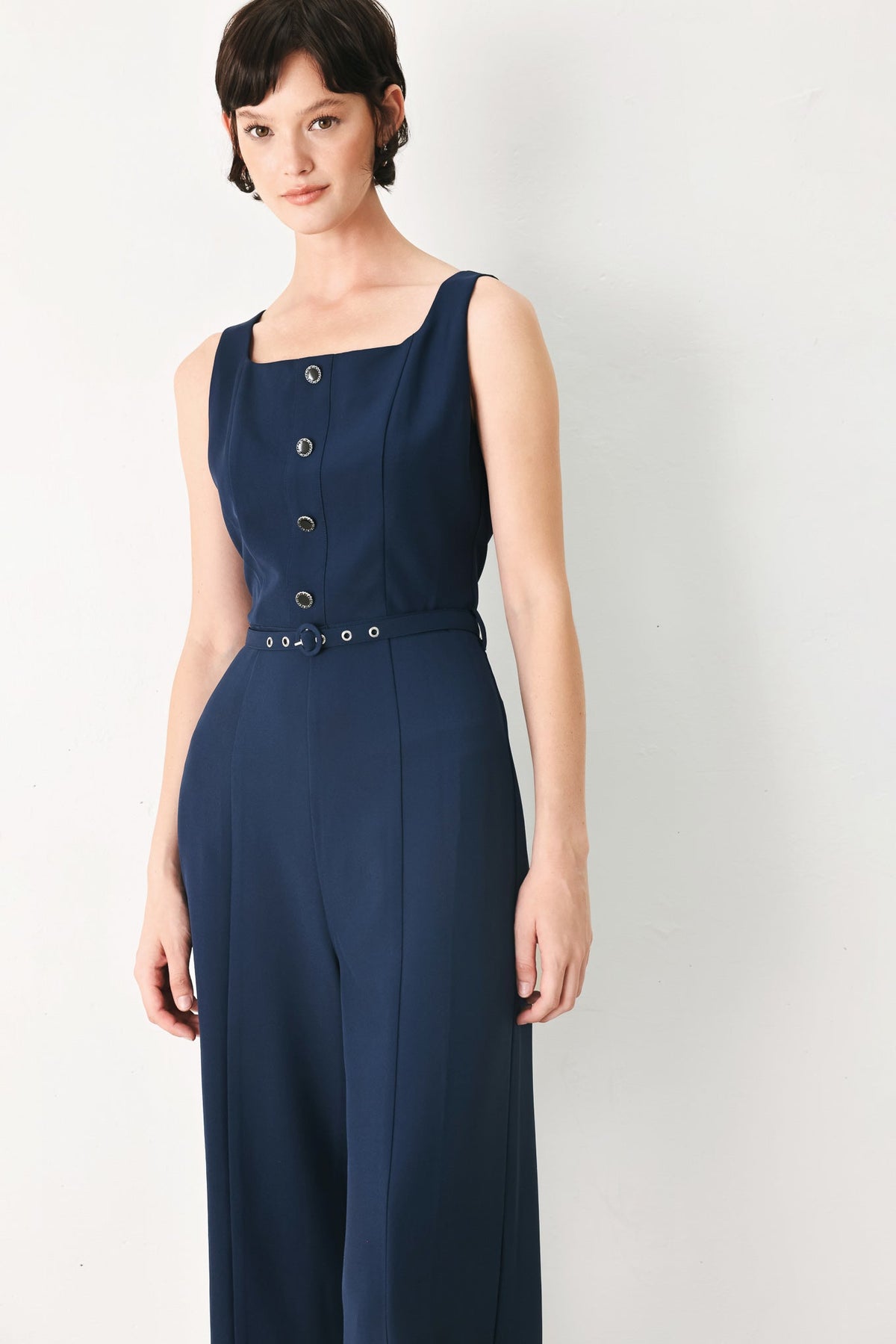 Woman wearing a navy blue sleeveless dress with buttons on a white background