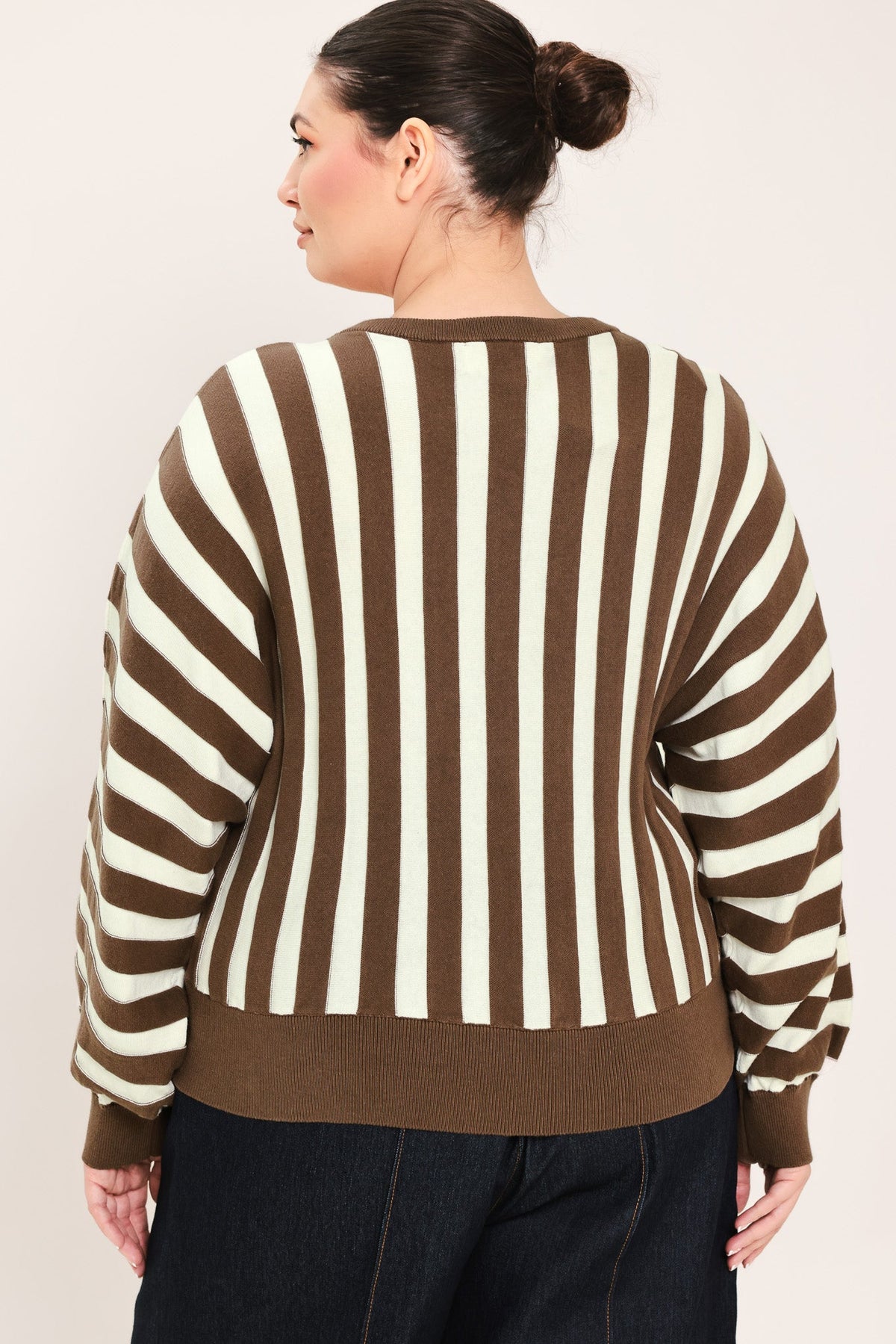 A woman shown from the back wearing a brown and cream striped sweater with balloon sleeves, paired with dark jeans, against a plain light beige background.