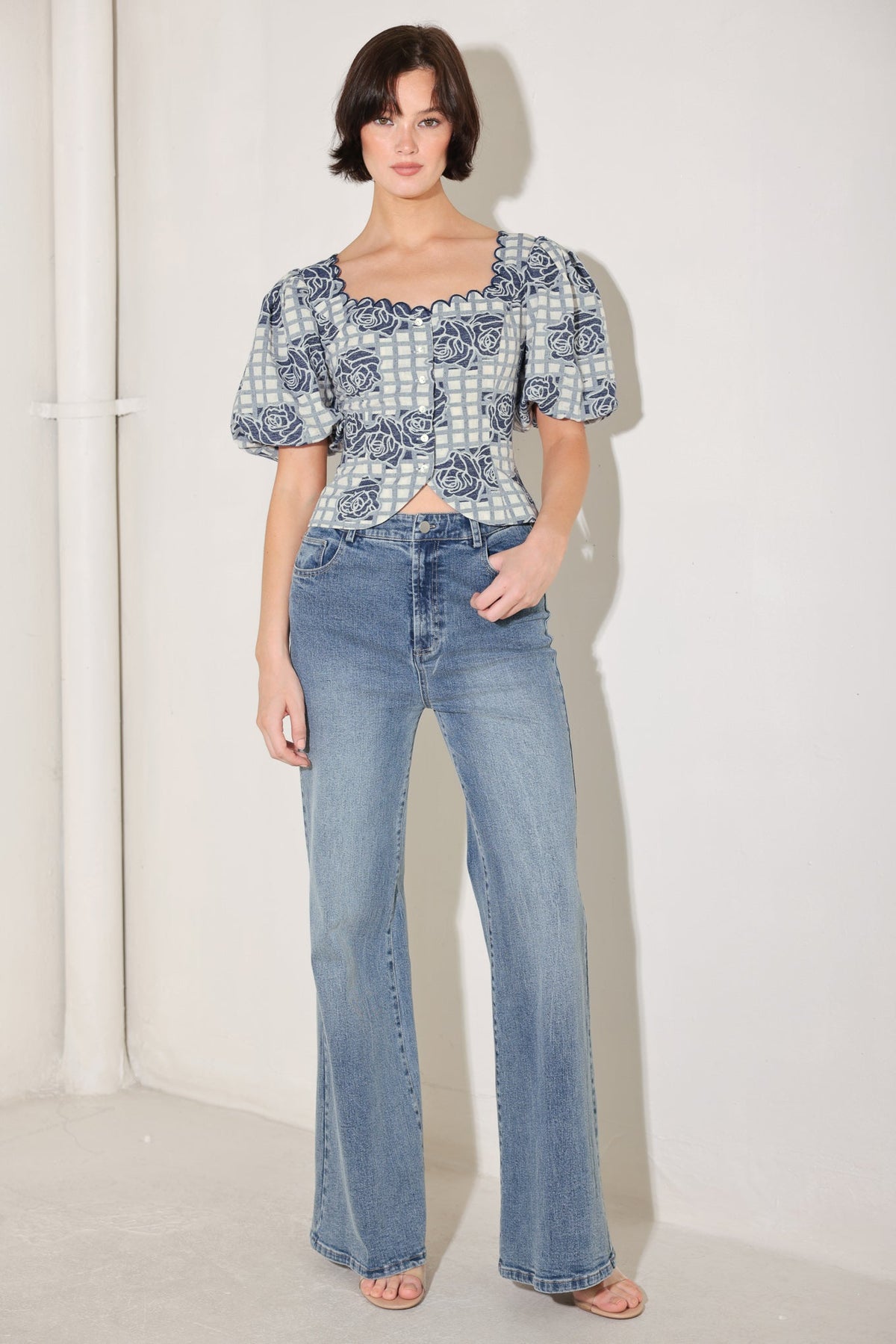 Woman wearing a patterned top and blue jeans against a white background