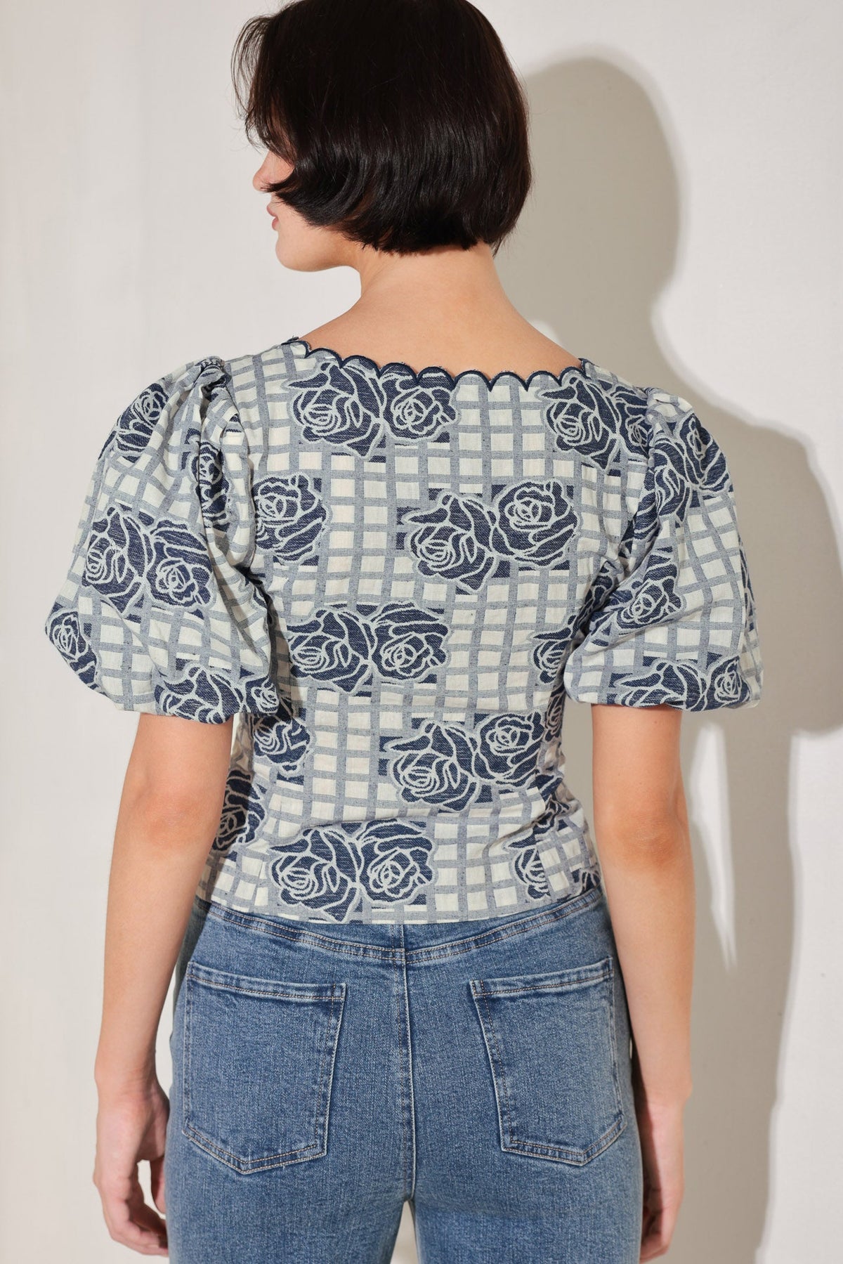 Person wearing a patterned blouse with puff sleeves and jeans against a plain background
