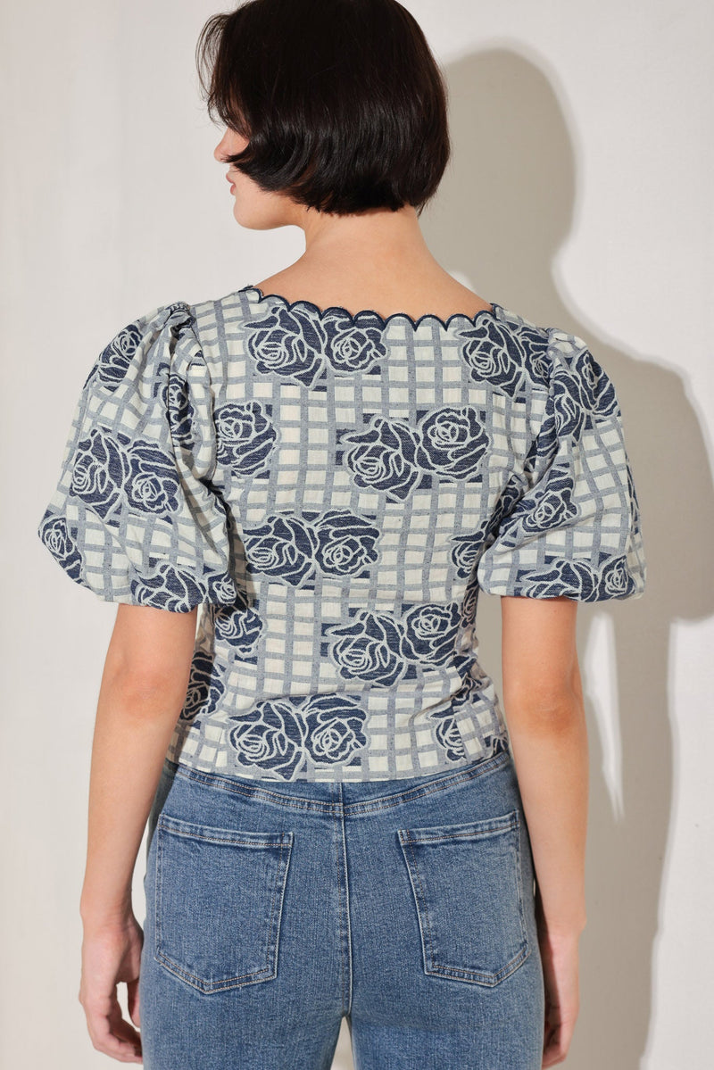 Person wearing a patterned blouse with puff sleeves and jeans against a plain background