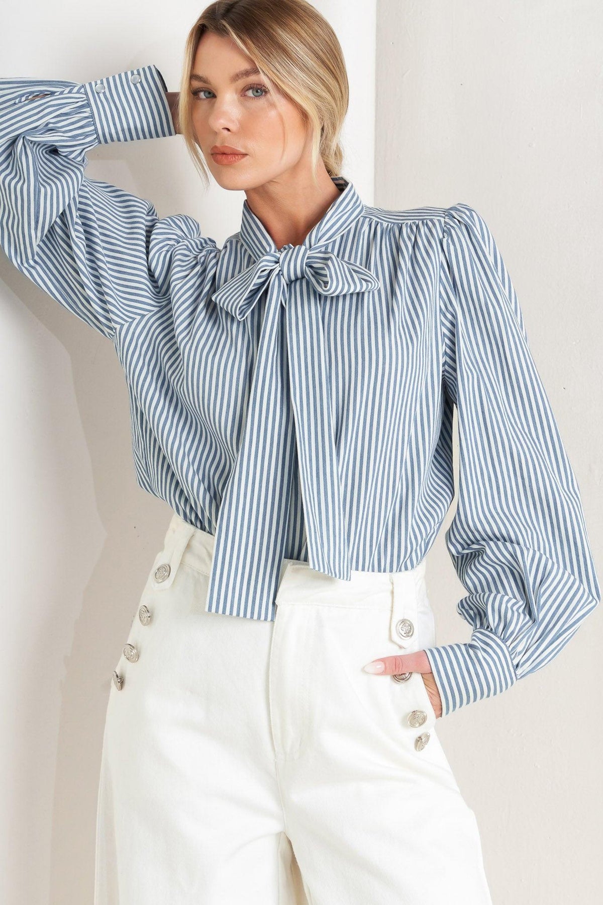 Woman wearing a blue and white striped blouse with a bow tie, standing against a plain background.