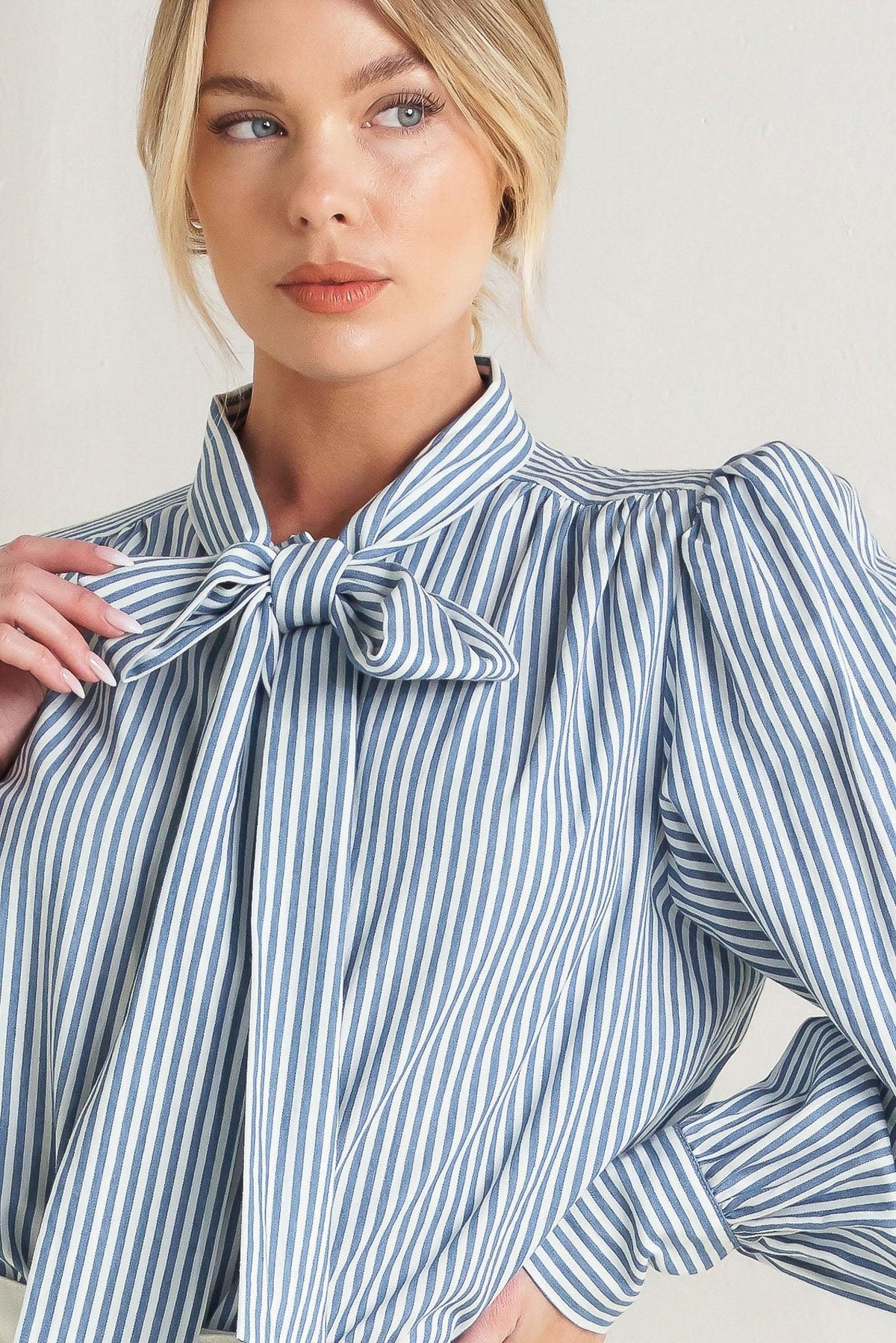 Woman wearing a blue and white striped blouse with a bow detail.