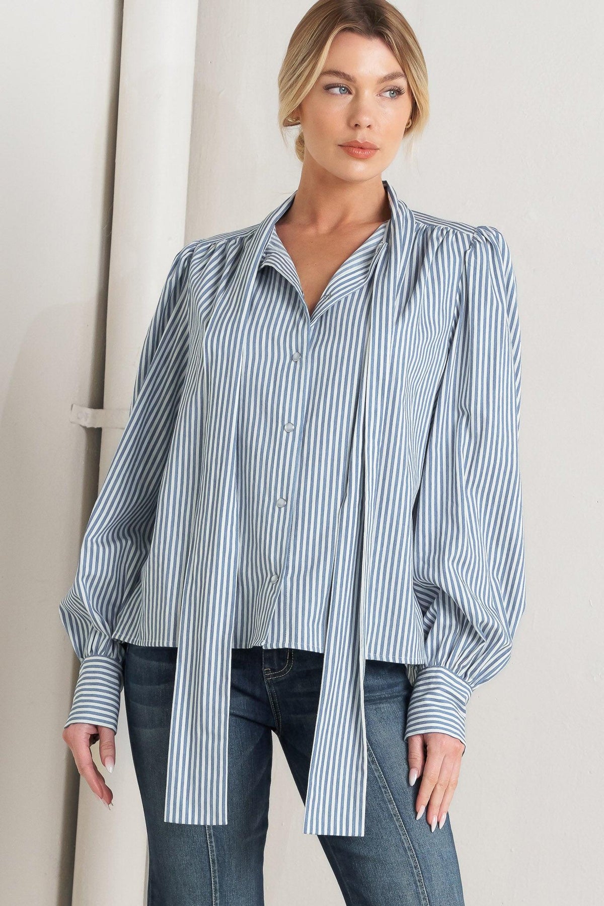 Woman wearing a blue and white striped shirt with puffed sleeves against a neutral background