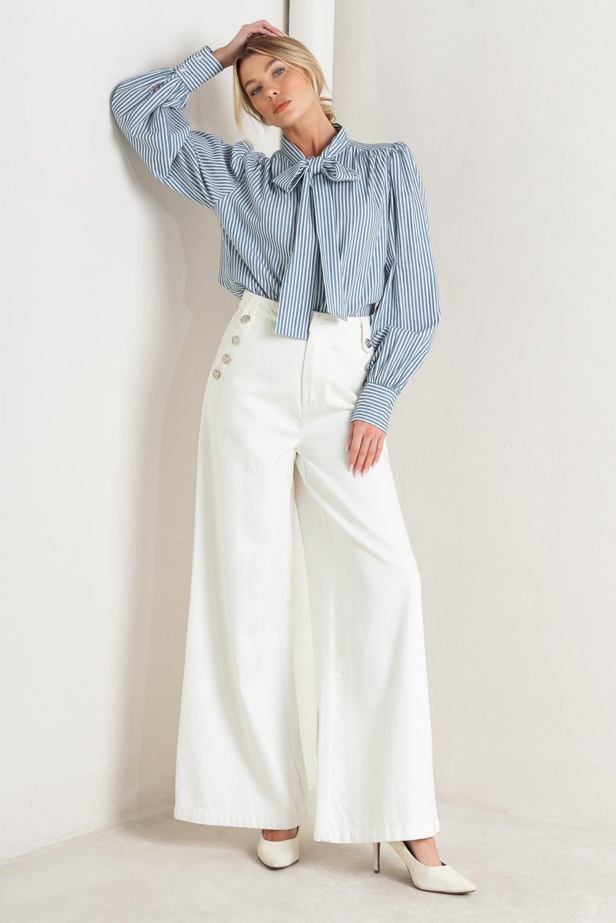 Woman wearing a blue striped shirt and white wide-leg pants against a light background