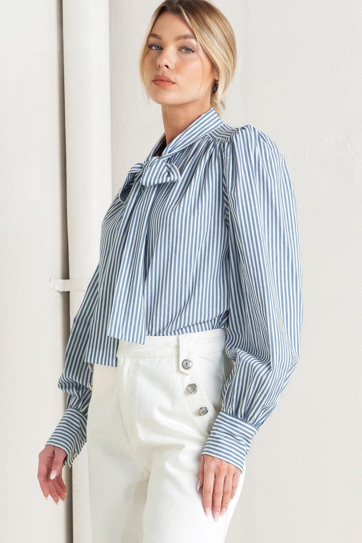 Woman wearing a blue and white striped blouse with a bow tie, standing against a plain background.