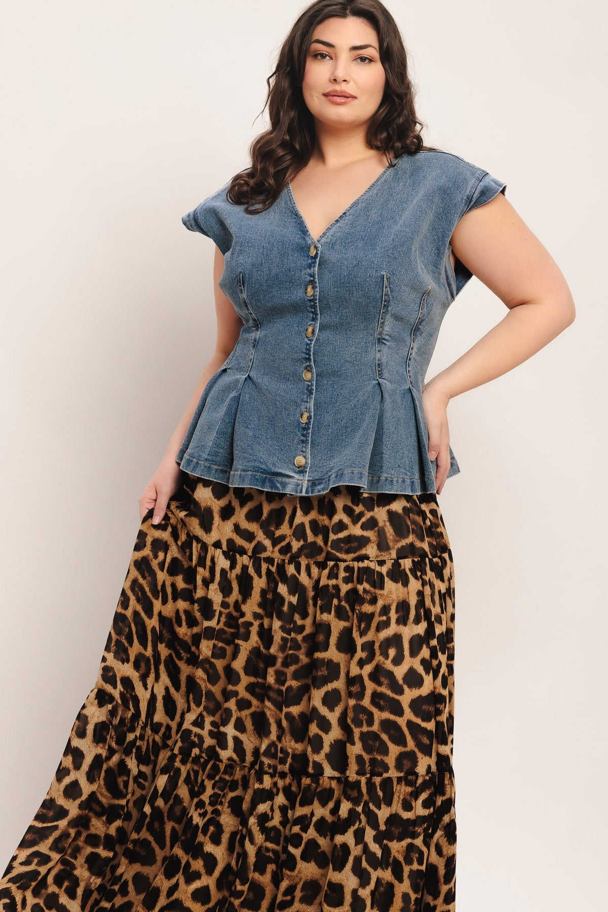Woman wearing a denim peplum top and leopard print skirt on a plain background