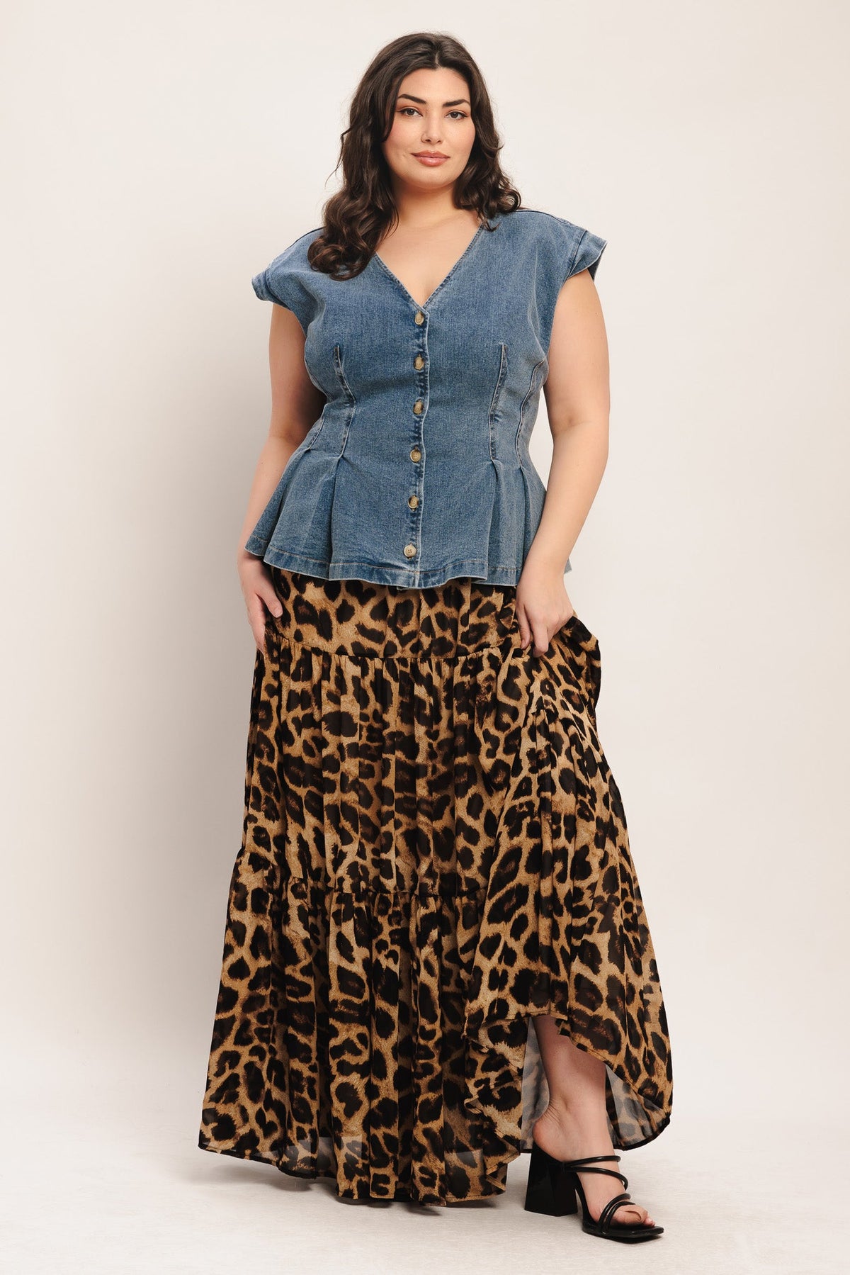 Woman wearing a denim peplum top and leopard print skirt on a plain background