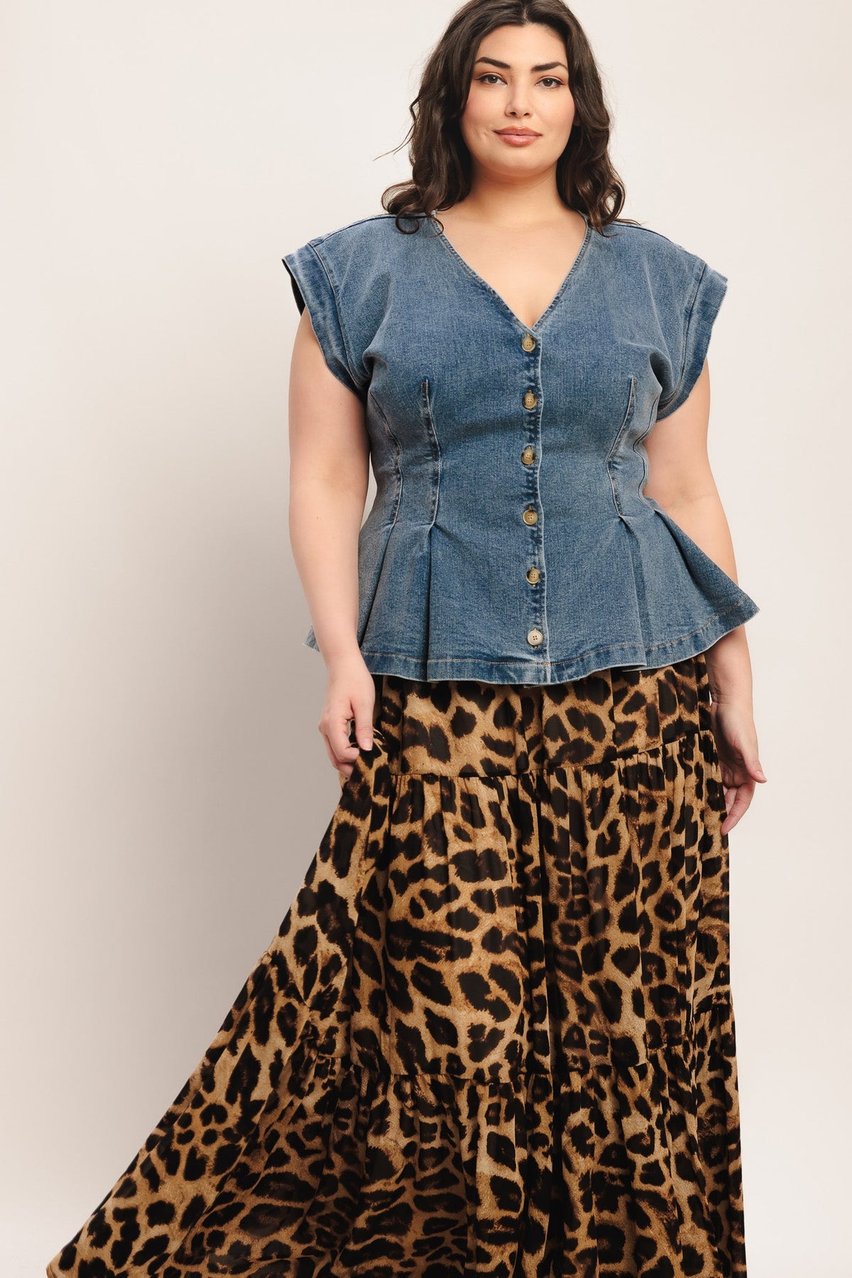 Woman wearing a denim peplum top and leopard print skirt on a plain background
