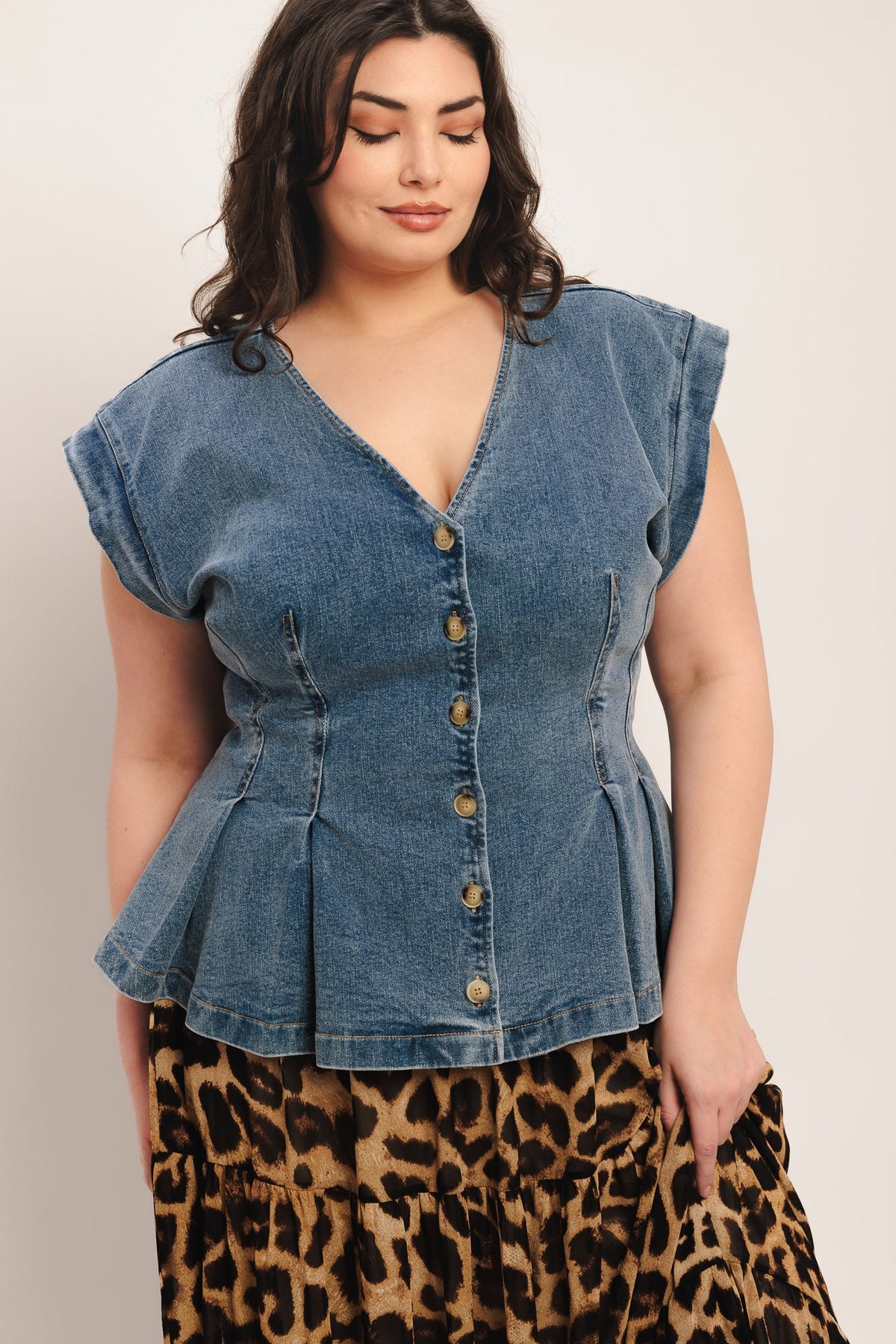 Woman wearing a denim peplum top with a leopard print skirt on a plain background
