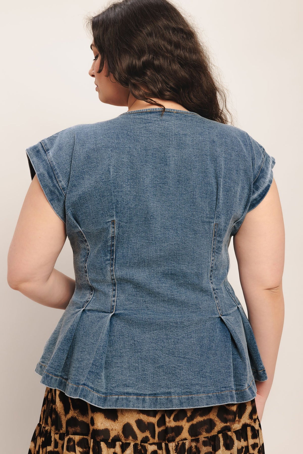 Person wearing a denim peplum top over a leopard print skirt on a plain background