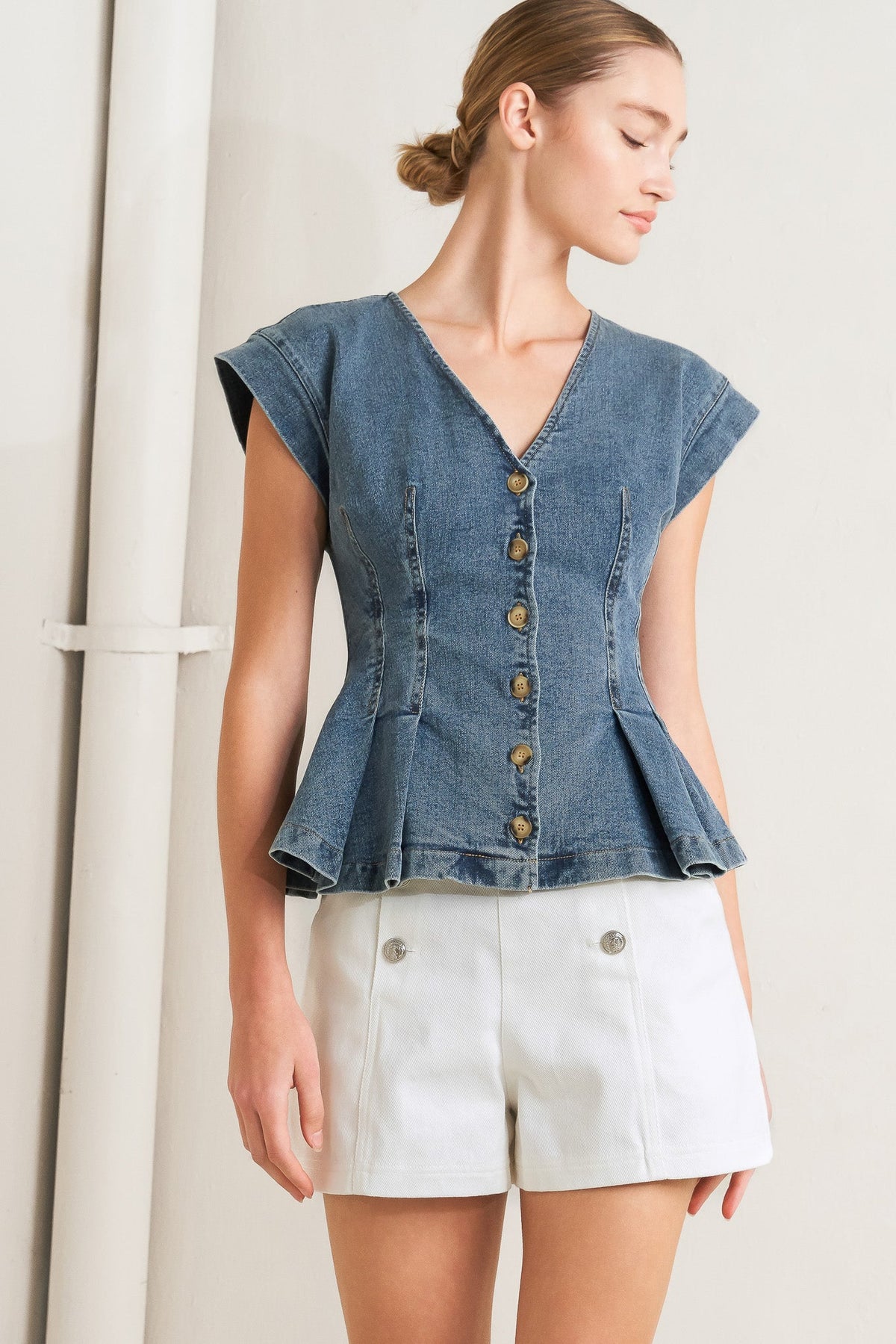 Woman wearing a denim peplum top and white shorts against a neutral background