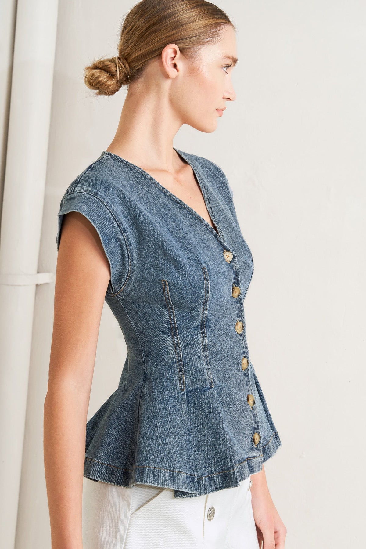 Woman wearing a denim vest with button details on a plain background