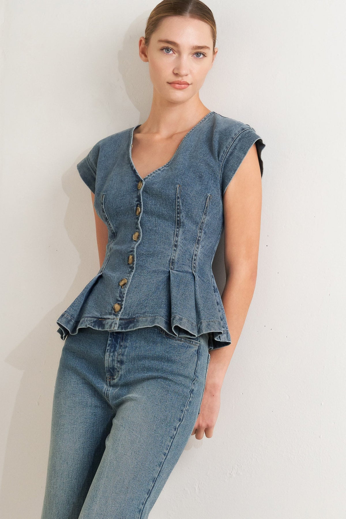 Woman wearing a denim peplum top and jeans against a white background