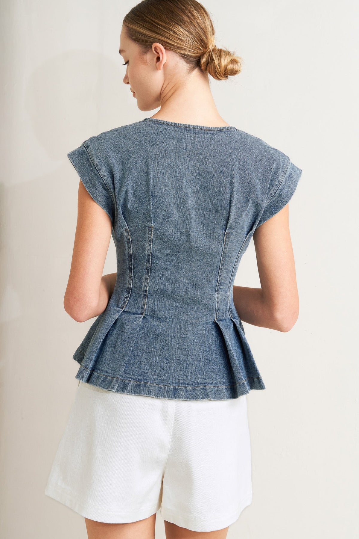Woman wearing a denim peplum top and white shorts on a plain background