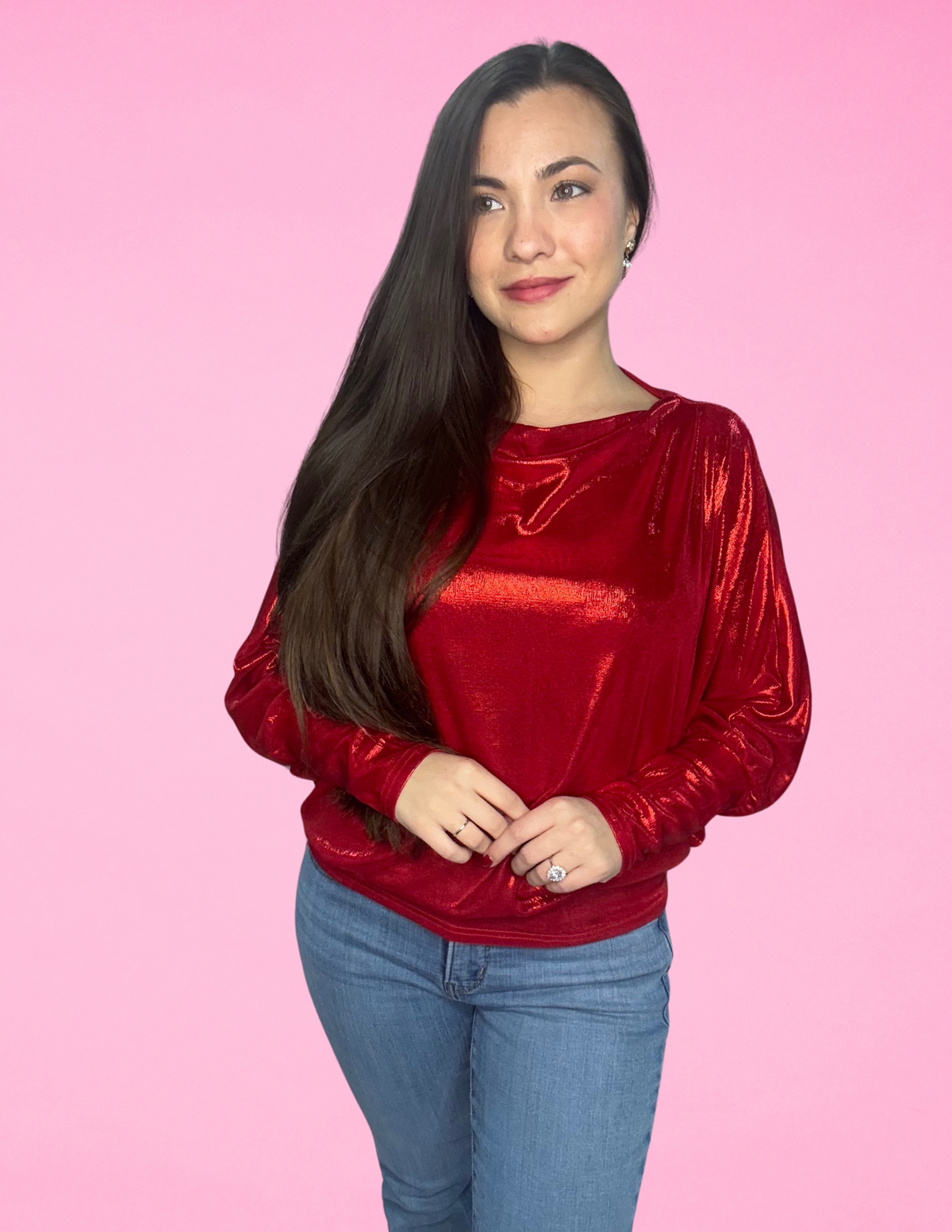 A woman wearing a red off-the-shoulder dolman long sleeve metallic foil knit top with blue jeans.
