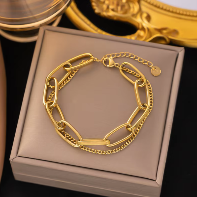 A gold chain bracelet with chunky interlocking links and a central bar, displayed on a beige jewelry box.