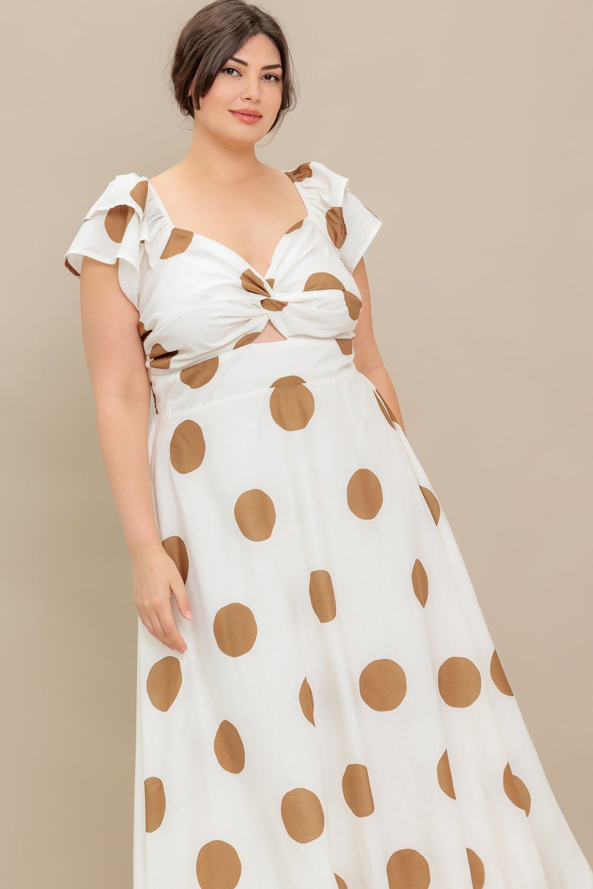 Woman wearing a white dress with brown polka dots against a beige background