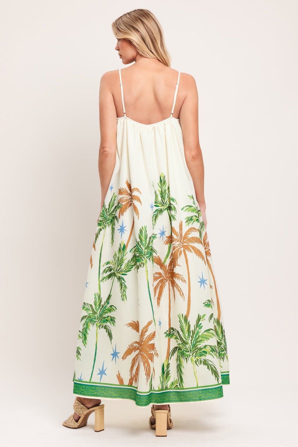 Woman wearing a white dress with palm tree print on a plain background