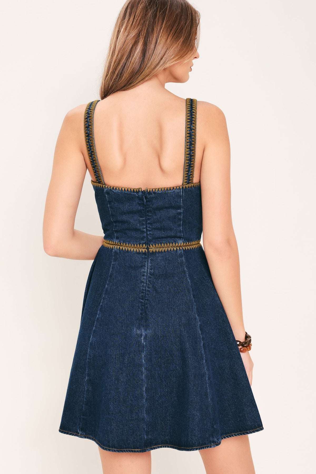 Woman wearing a blue denim dress with thin straps on a plain background