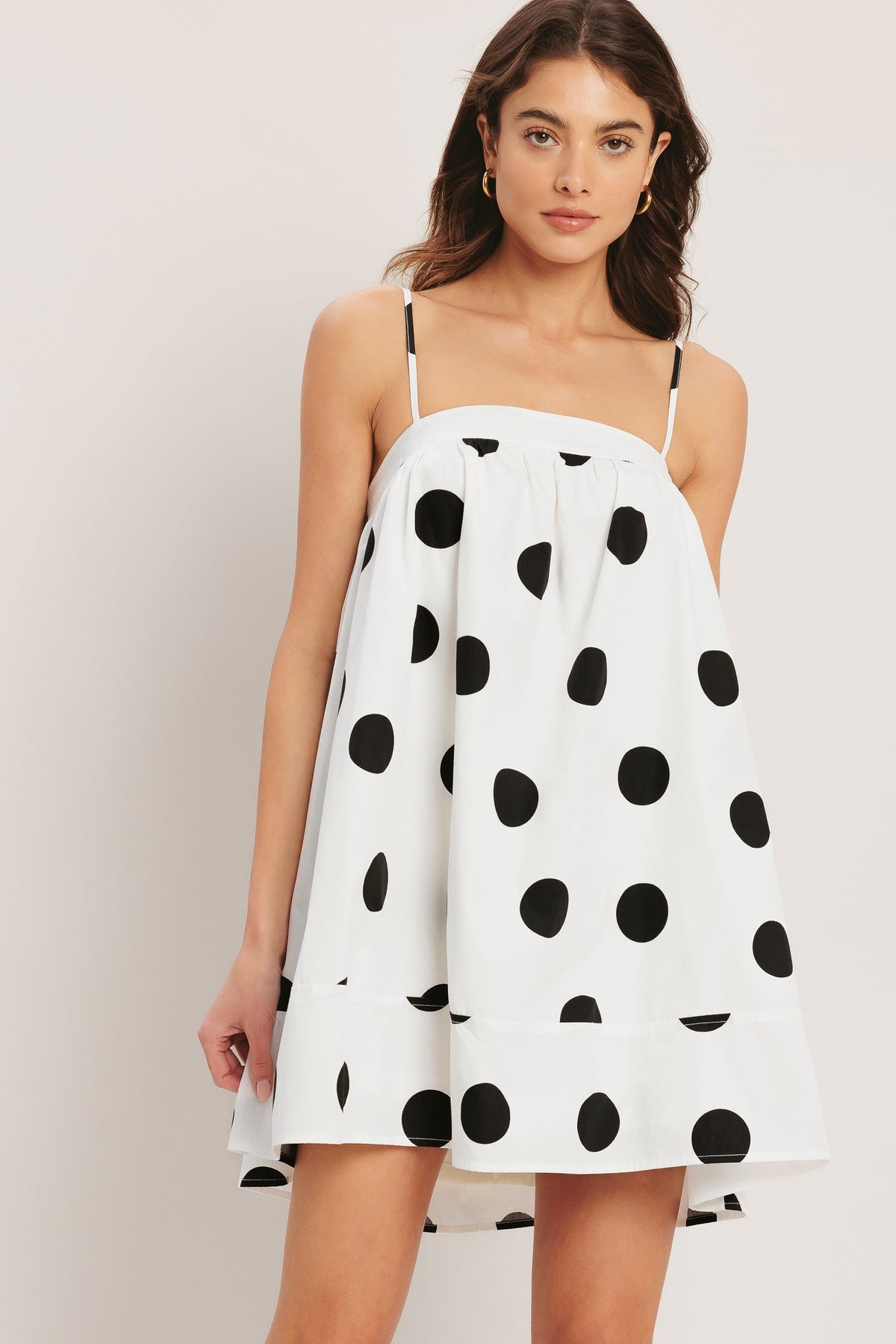 Woman wearing a white dress with black polka dots against a plain background
