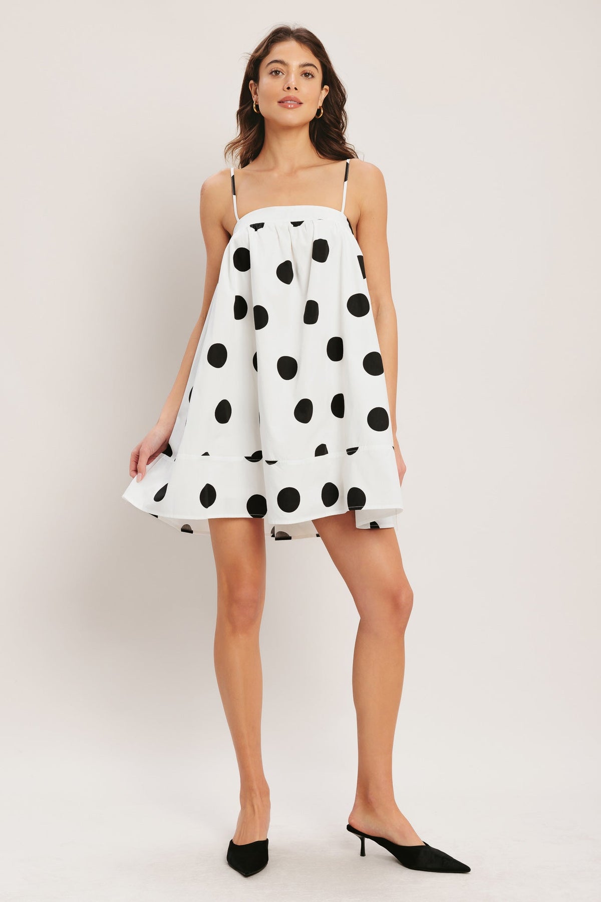 Woman wearing a white dress with black polka dots on a plain background