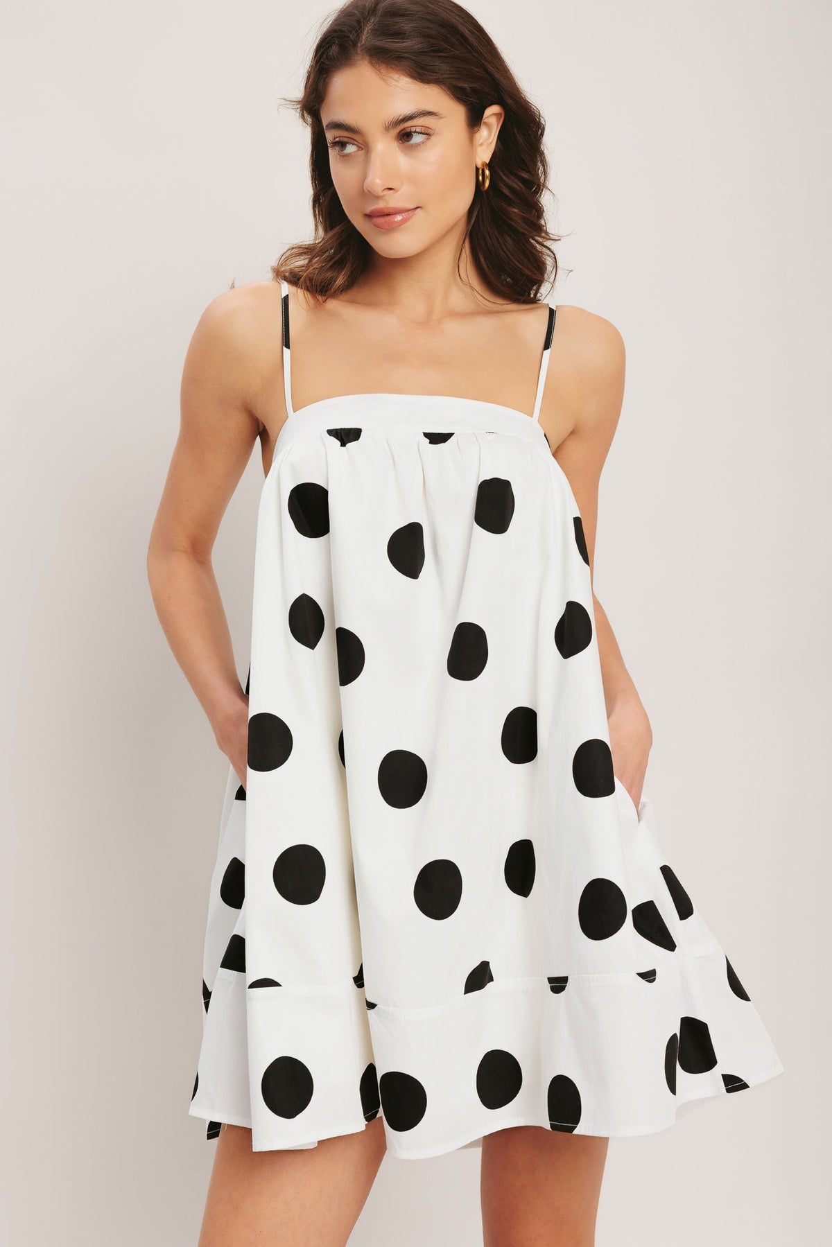 Woman wearing a white dress with black polka dots against a plain background