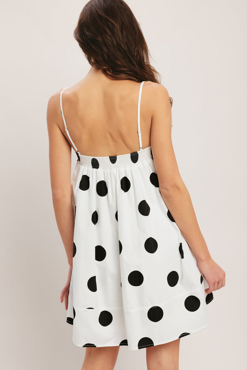 Woman wearing a white dress with black polka dots against a plain background