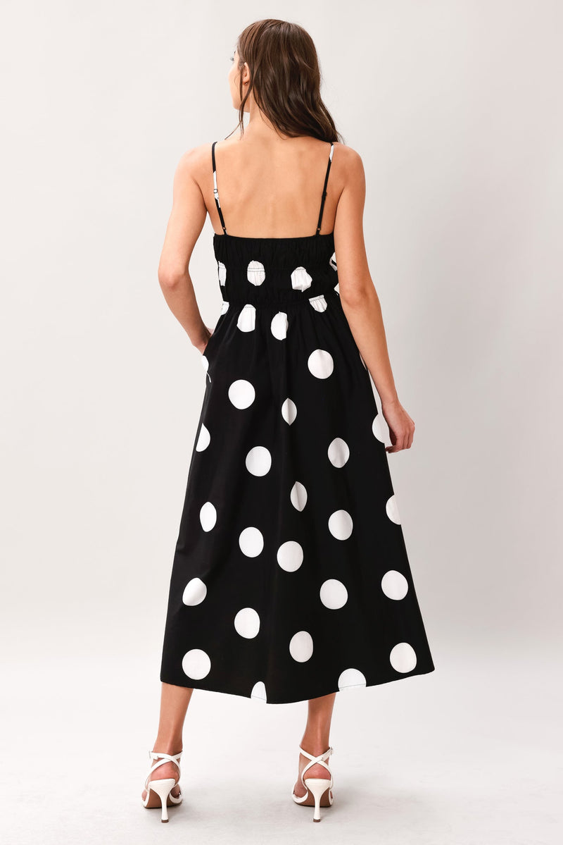 Woman wearing a black dress with white polka dots on a plain background