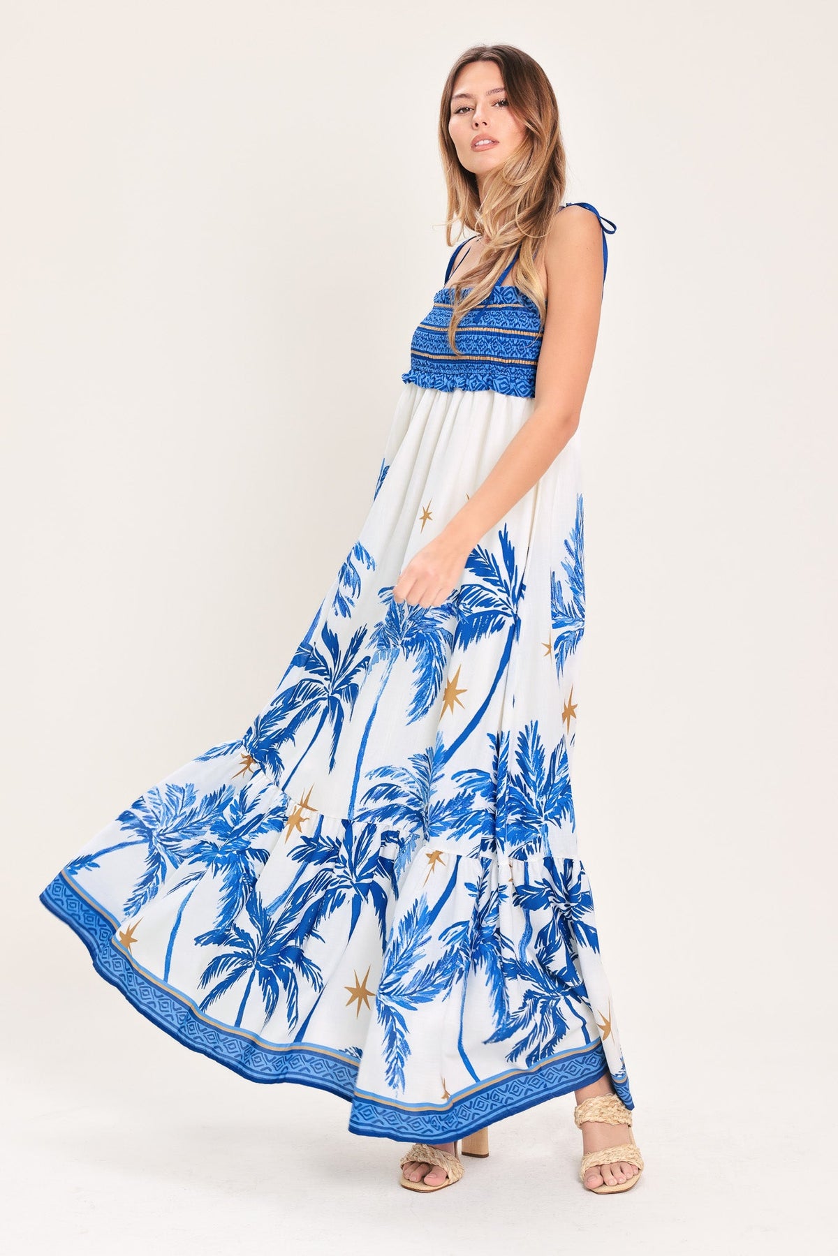 Woman wearing a blue and white dress with palm tree pattern on a white background
