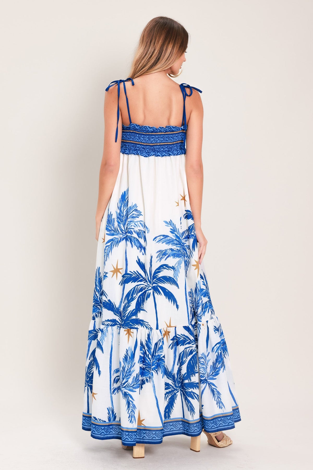 Woman wearing a blue and white palm tree patterned dress on a plain background