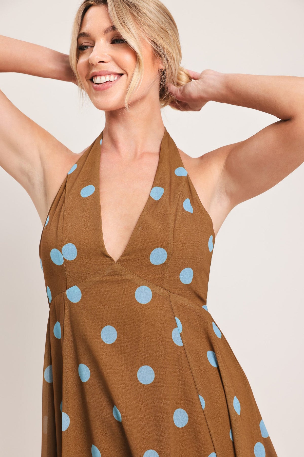 Woman wearing a brown dress with blue polka dots against a plain background