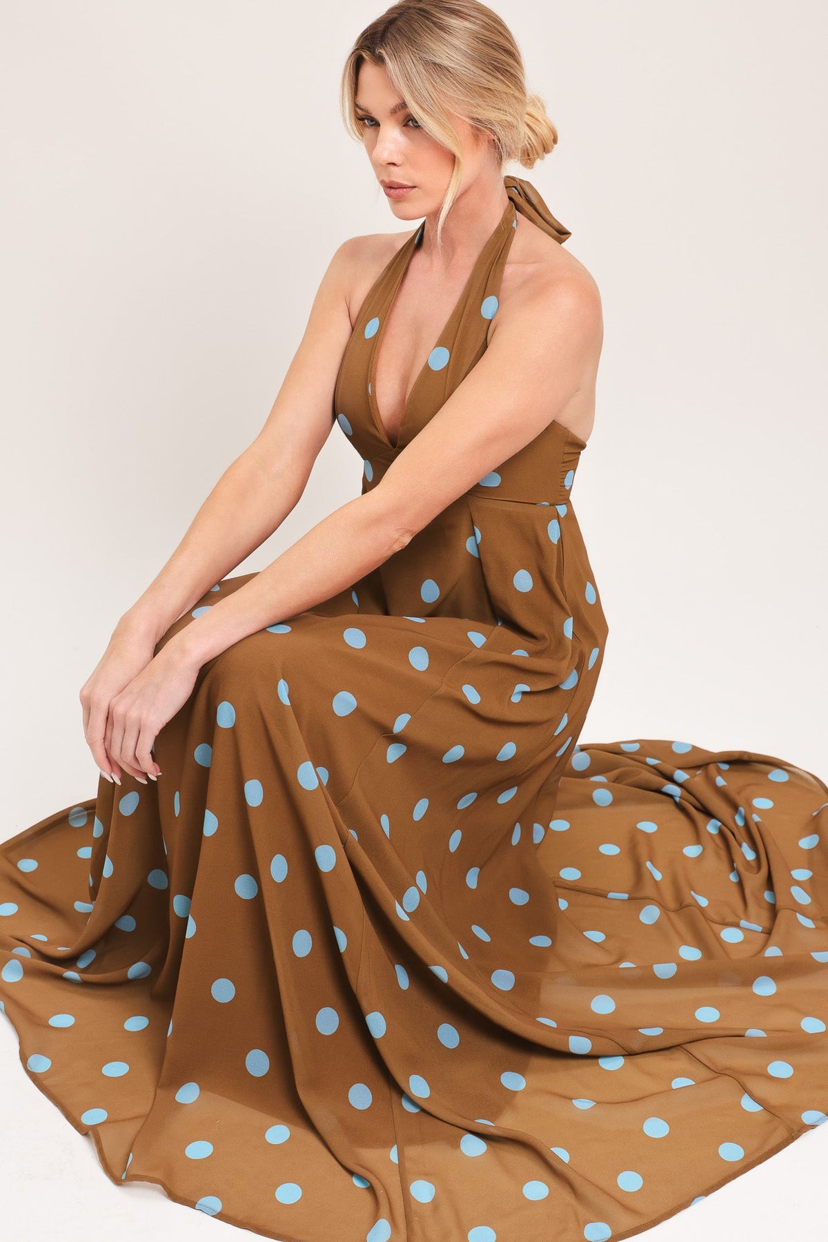 Woman wearing a brown dress with blue polka dots on a plain background