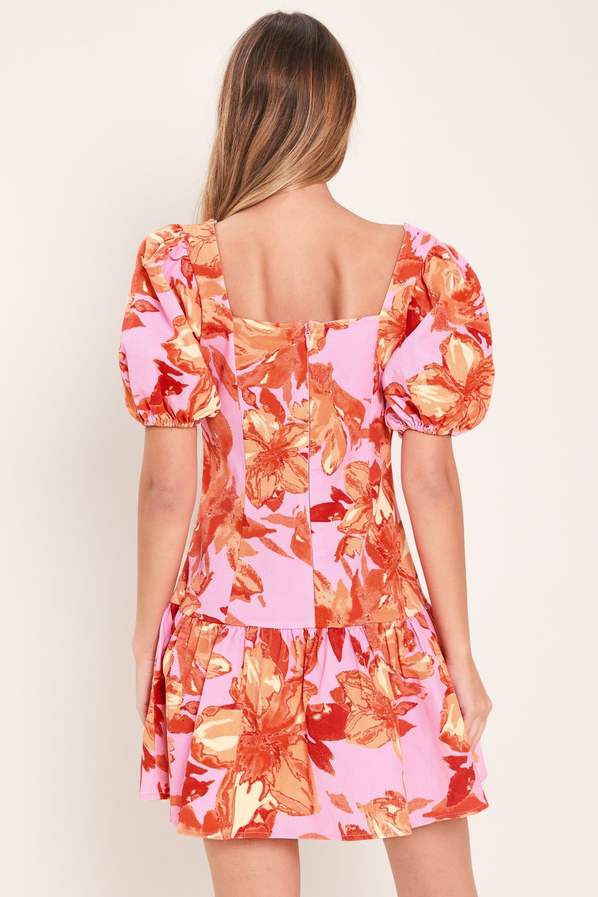 Woman wearing a colorful floral dress with puff sleeves on a plain background