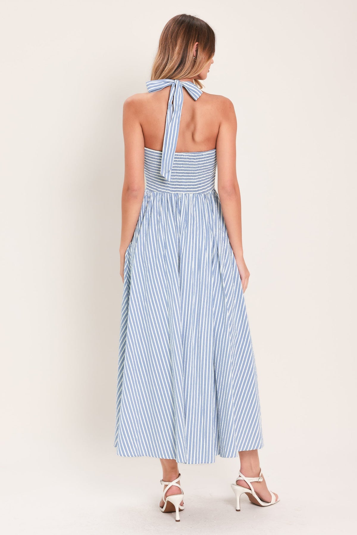 Woman wearing a blue and white striped dress with a halter neck design on a light background