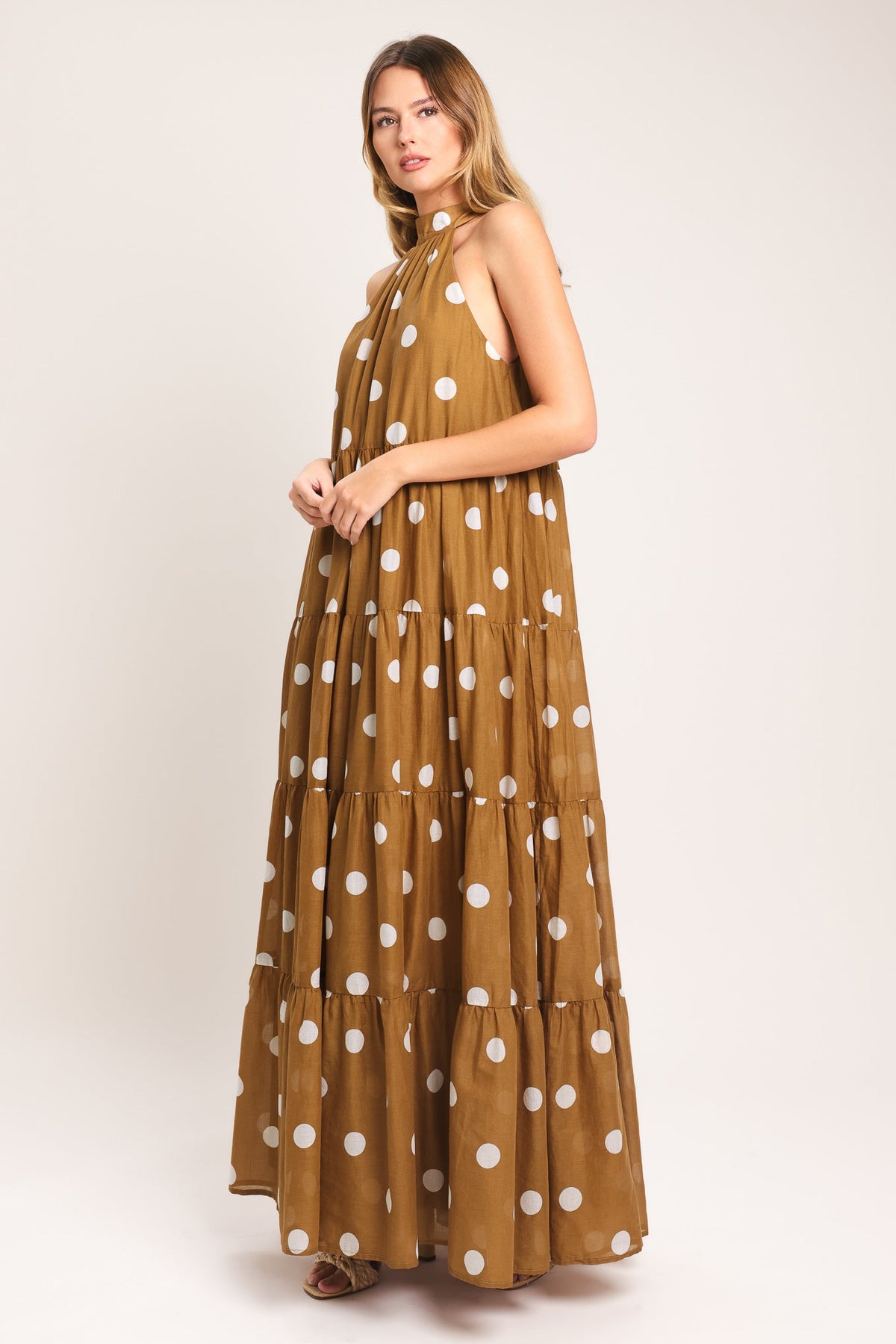 Woman wearing a long brown dress with white polka dots on a white background