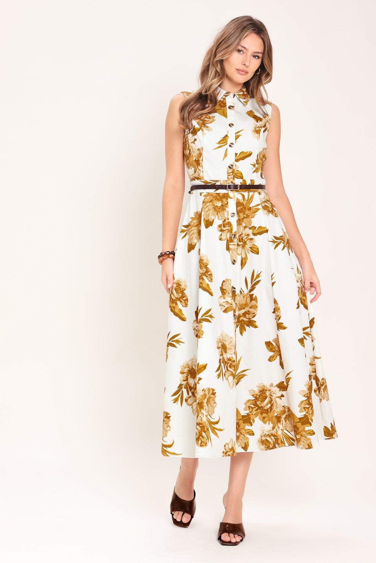 Woman wearing a white dress with gold floral pattern on a plain background