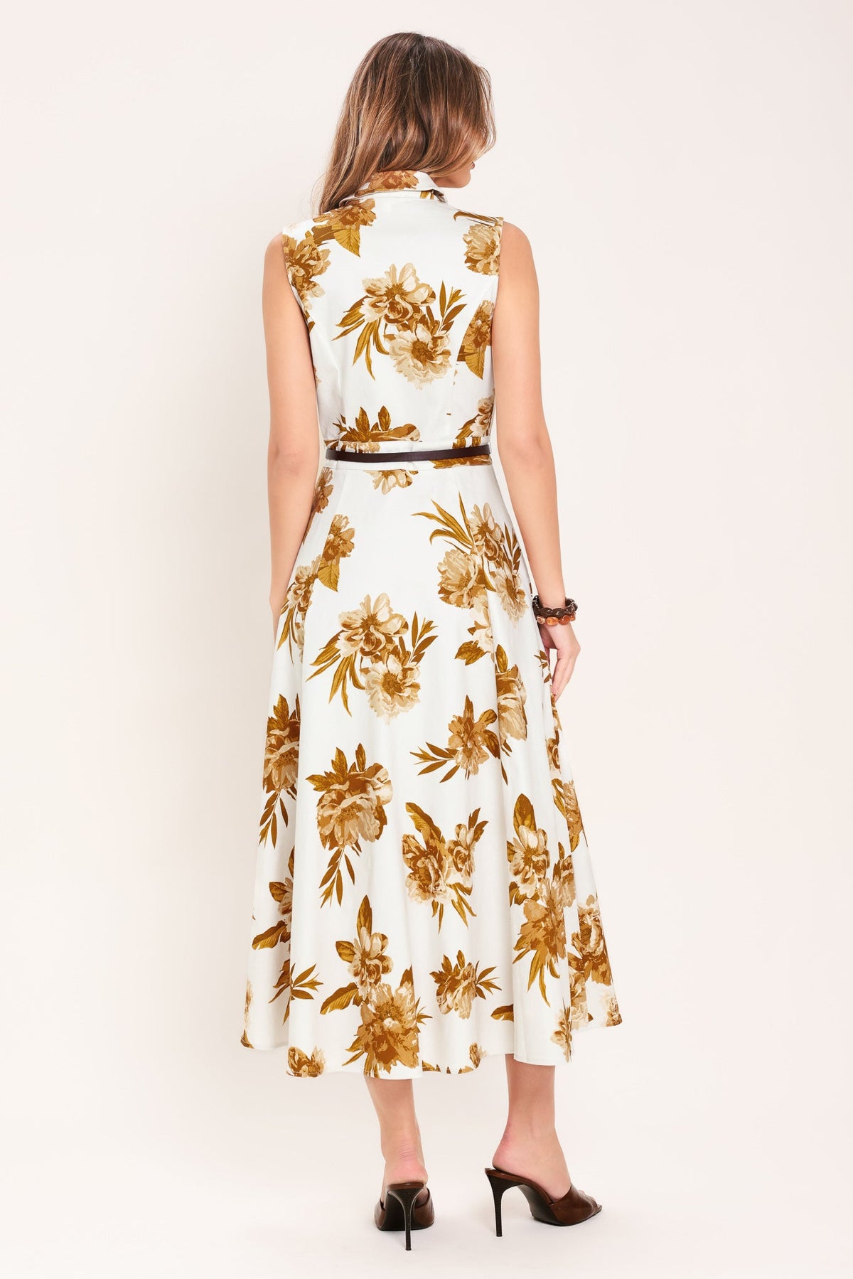 Woman wearing a white dress with gold floral pattern on a plain background