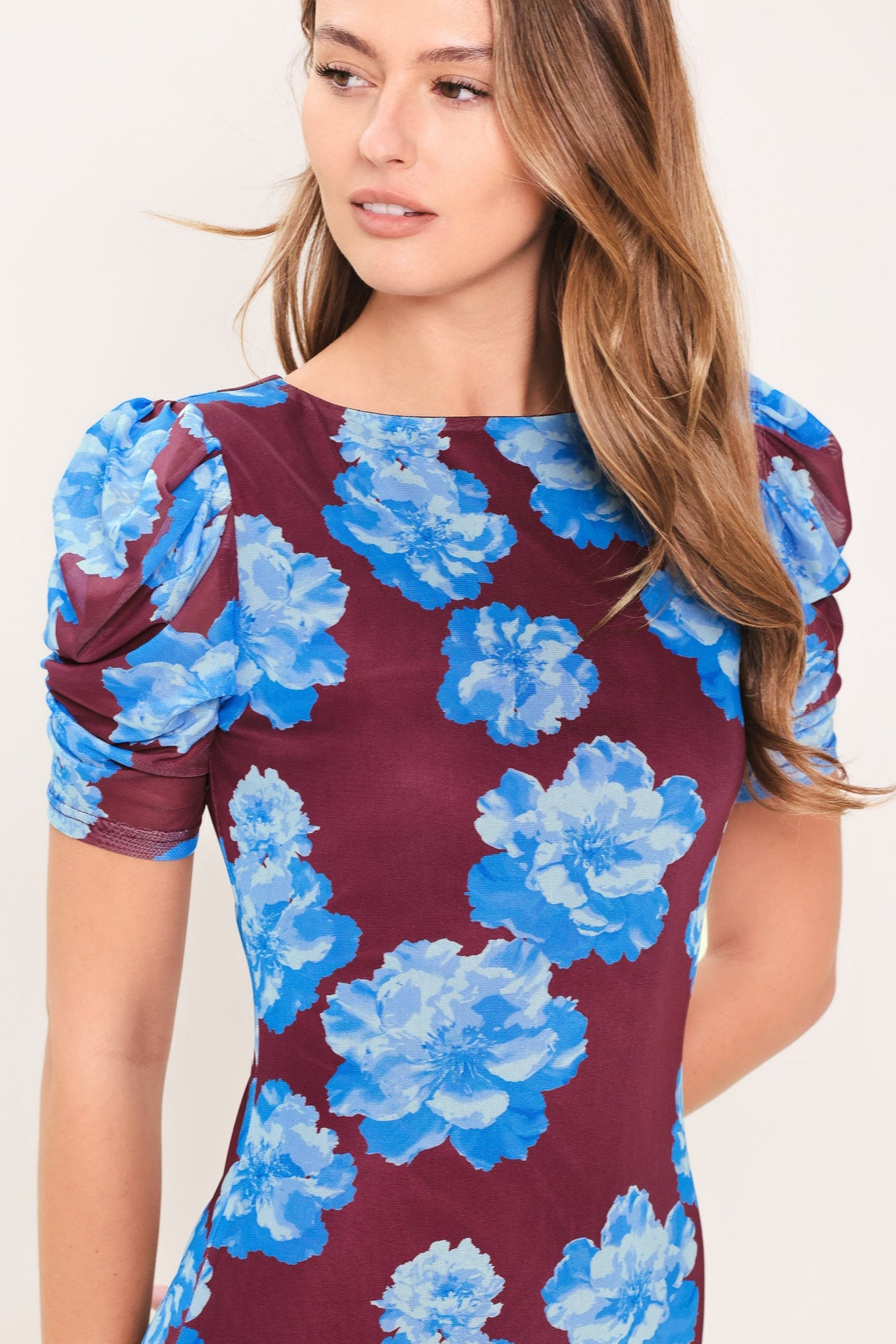 Woman wearing a dress with blue floral pattern on a plain background