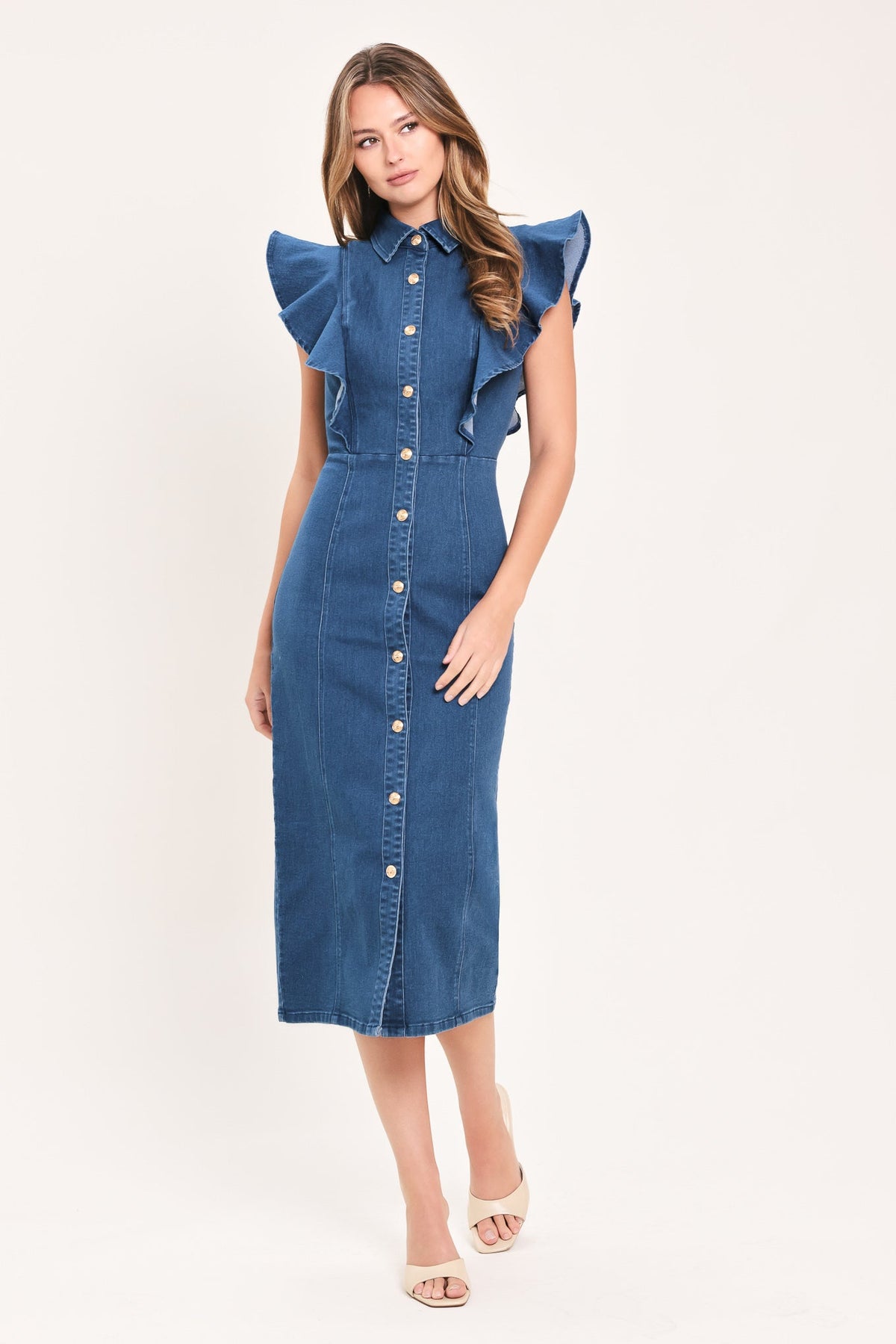 A woman modeling a blue denim midi dress with ruffled cap sleeves, a pointed collar, and a front button placket, photographed against a plain light background.