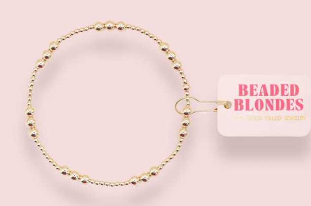 Gold beaded bracelet on a pink background with 'Beaded Blondes' label.