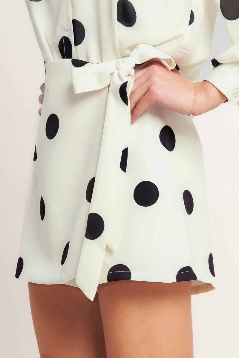White dress with black polka dots and a tie waist on a light background