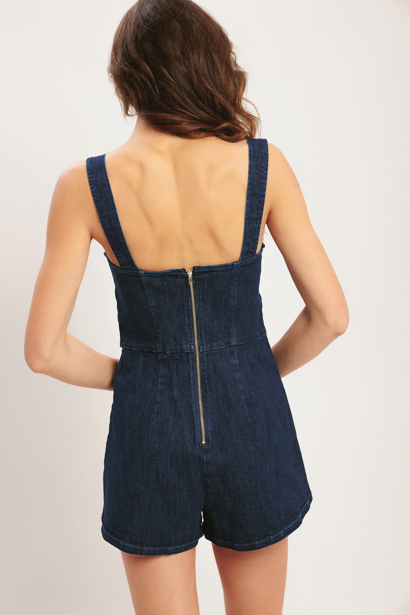 Person wearing a blue denim romper on a plain background