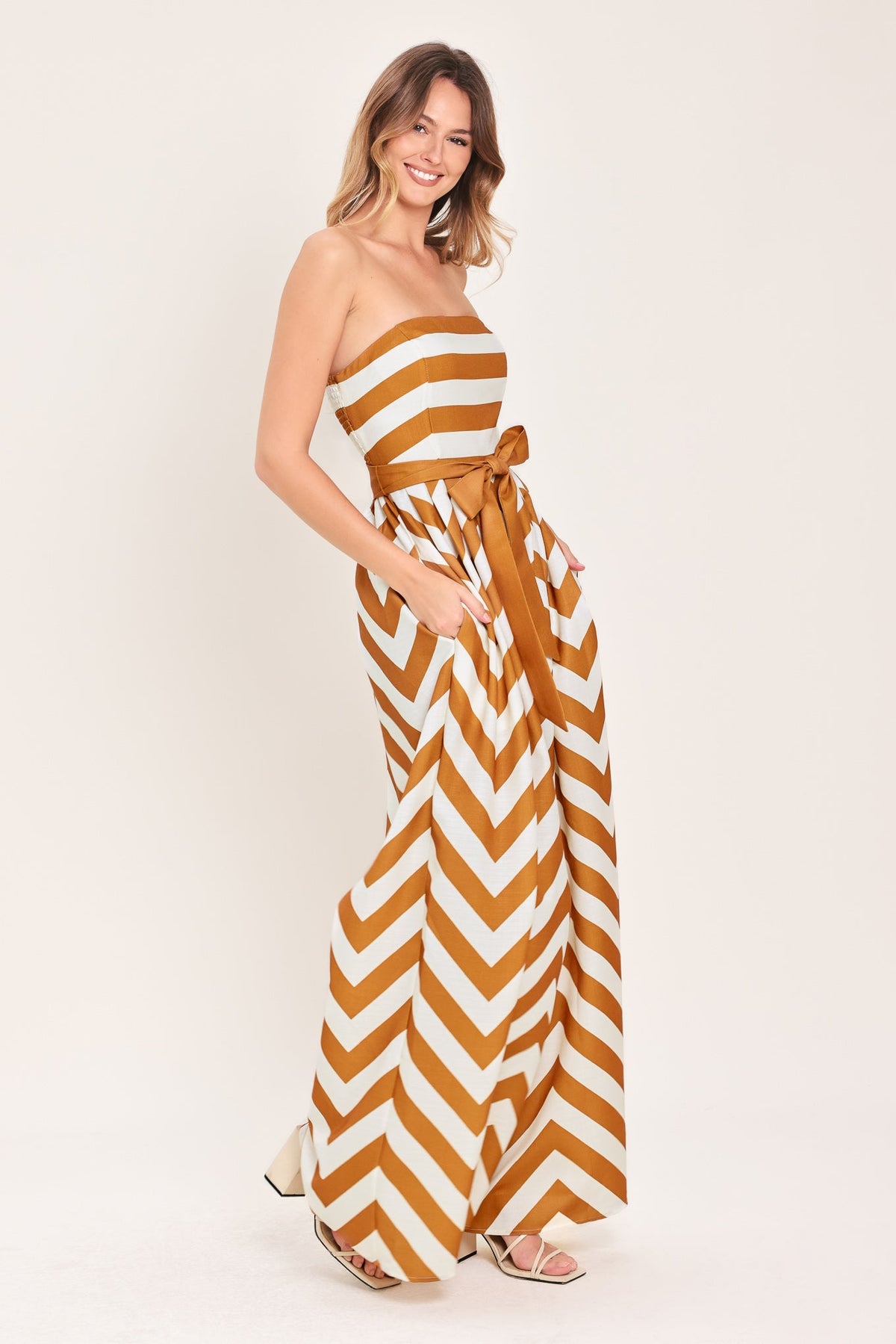 Woman wearing a strapless, long chevron-patterned dress on a white background