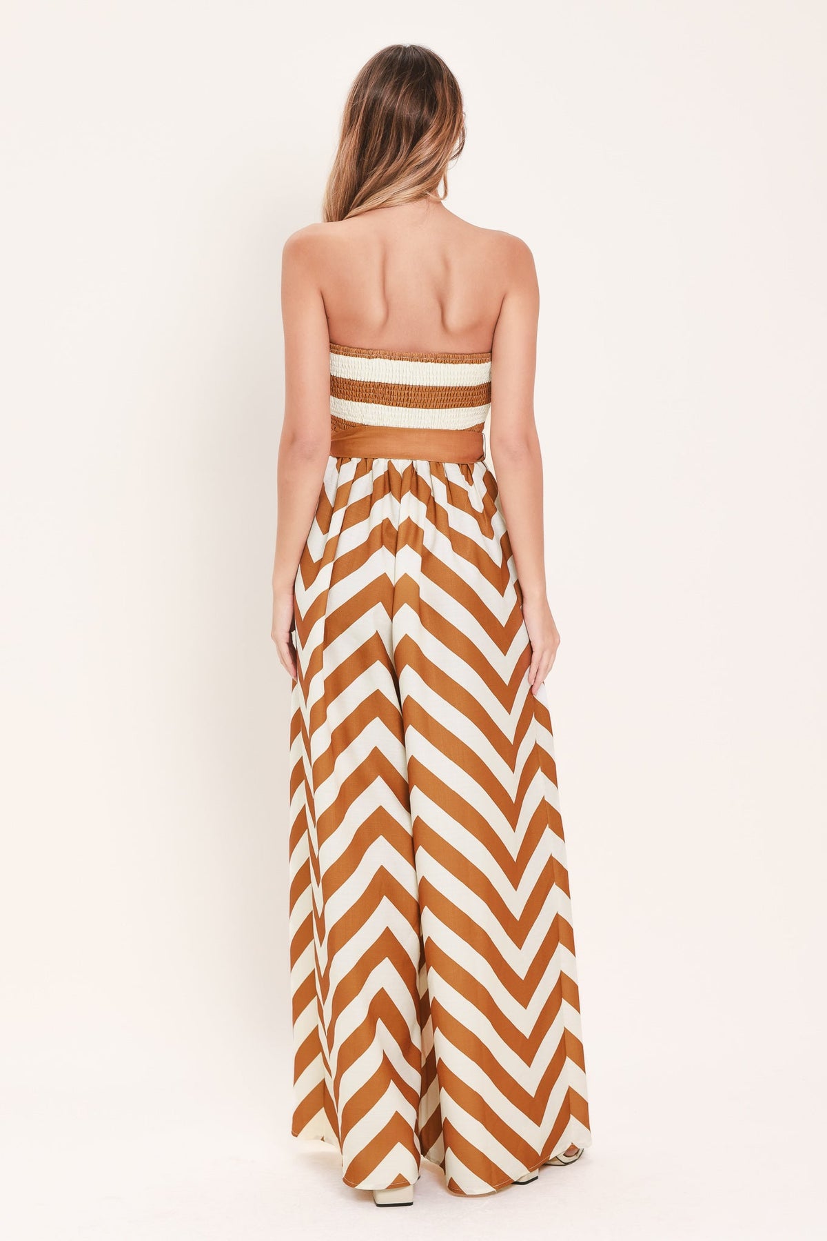 Woman wearing a strapless brown and white chevron dress on a white background