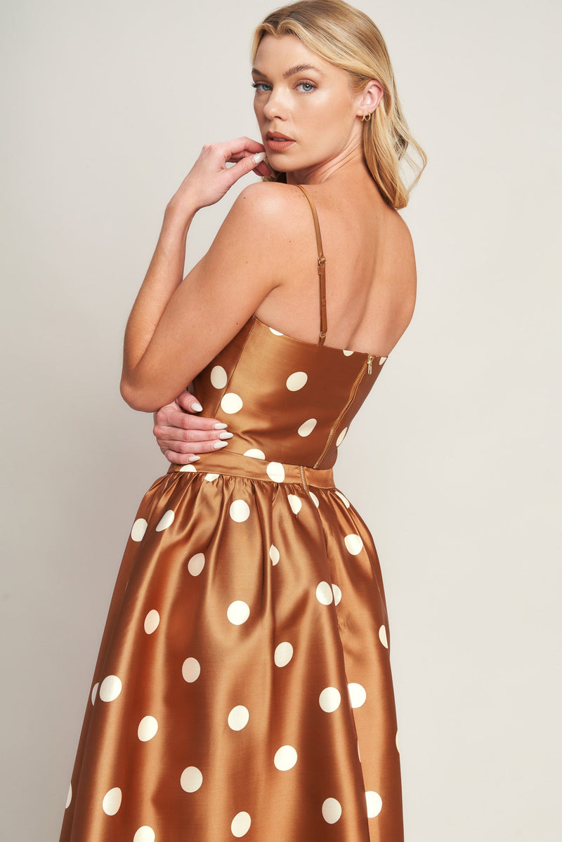 Woman wearing a gold satin dress with white polka dots on a plain background