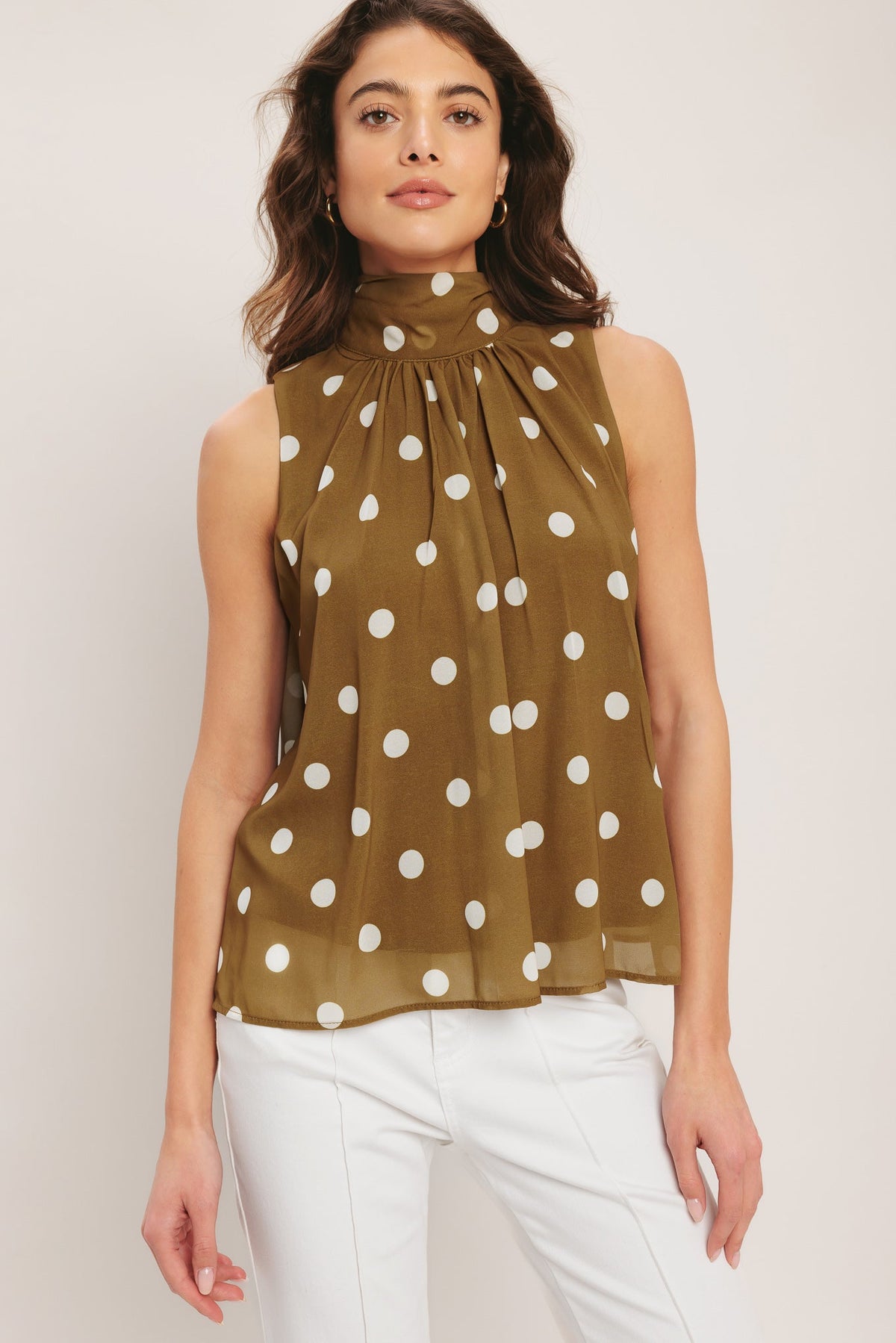 Woman wearing a green sleeveless top with white polka dots and white pants on a light background