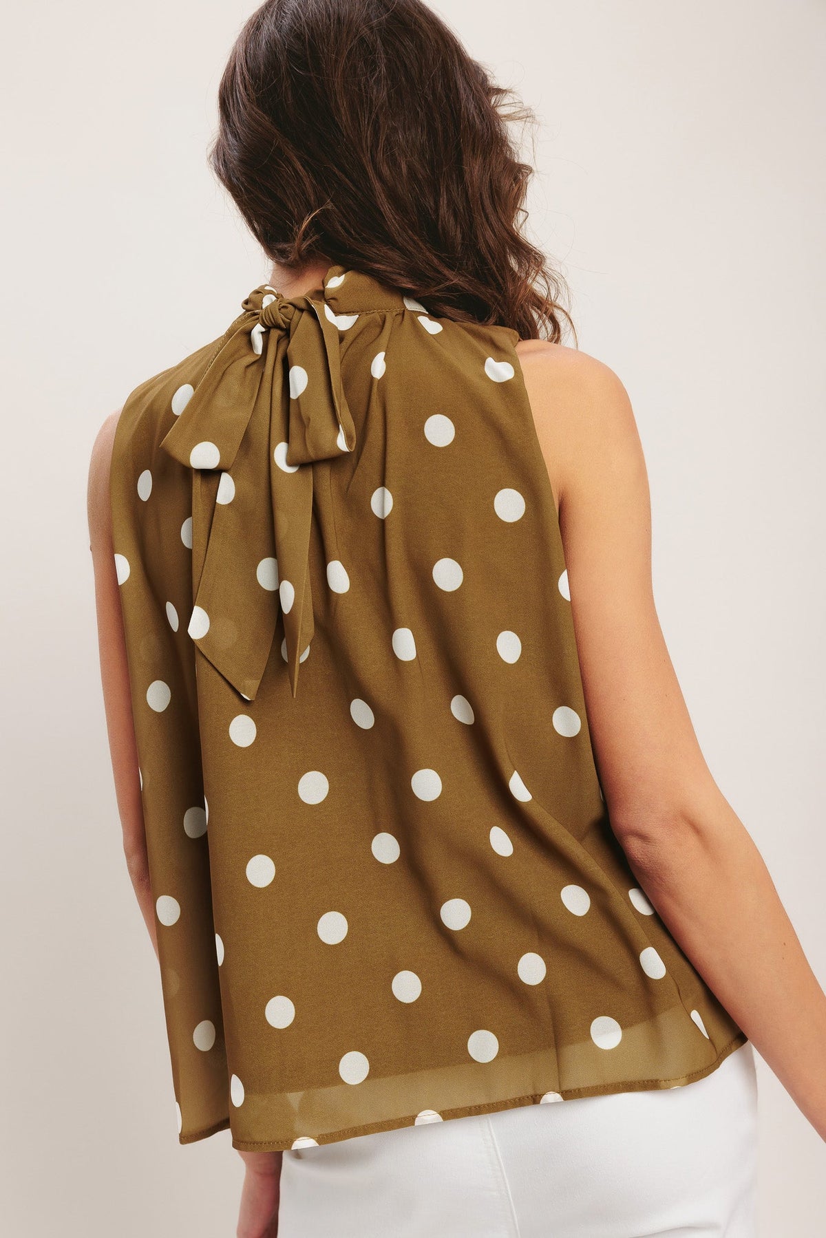 Woman wearing a brown sleeveless top with white polka dots on a plain background