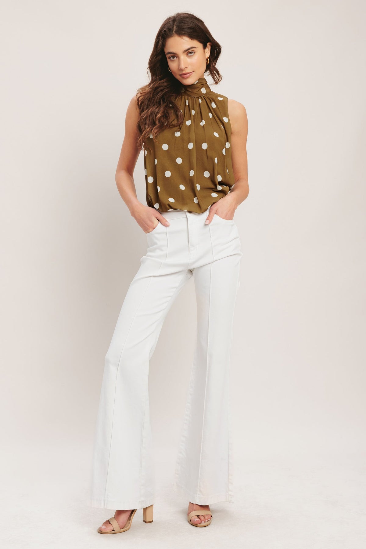 Woman wearing a polka dot top and white pants against a plain background